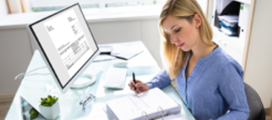Person working at a desk with computer and documents, illustrating article on HR system costs and budgeting for 2025."